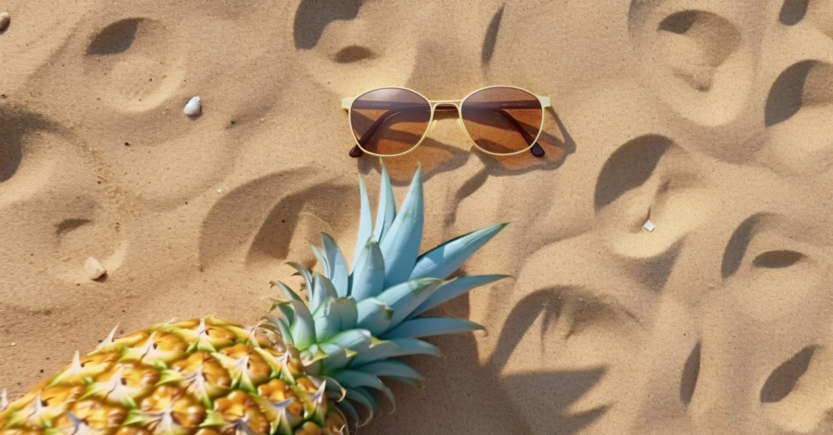 Piña partida por la mitad y gafas de sol guardadas en la arena 176
