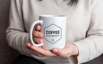 Taza blanca en manos femeninas con maqueta de logo