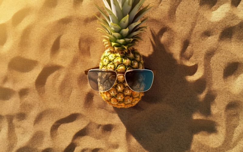 Ananas tagliato a metà e un occhiale da sole tenuto sulla sabbia 181